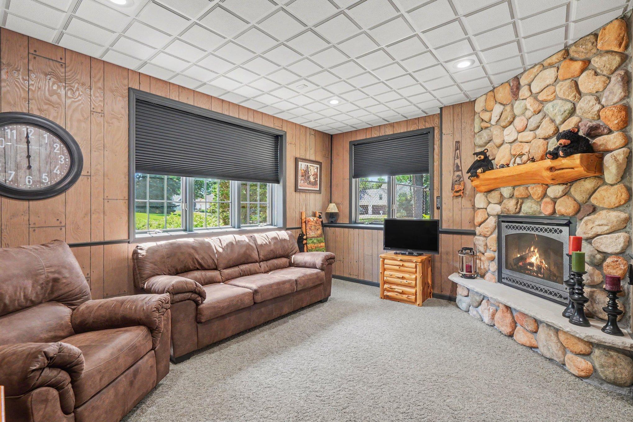 A cozy lower-level retreat features a dramatic stone fireplace, warm wood finishes and large windows overlooking the yard. It’s an inviting spot to unwind, watch a movie or enjoy a quiet evening by the fire. Wood-burning - sellers have never used.