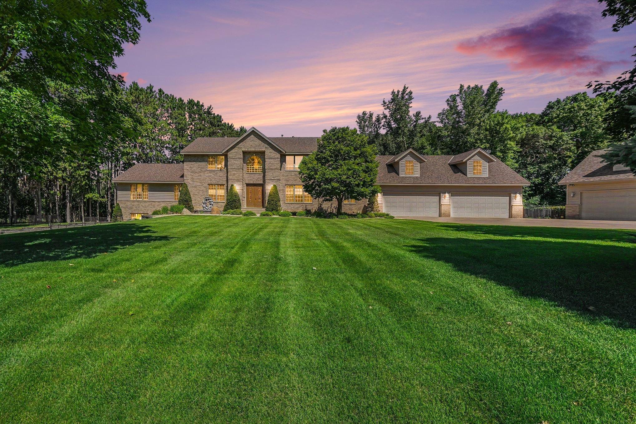 A breathtaking twilight view highlights the home’s expansive presence, beautifully manicured lawn and impressive setting surrounded by mature trees.