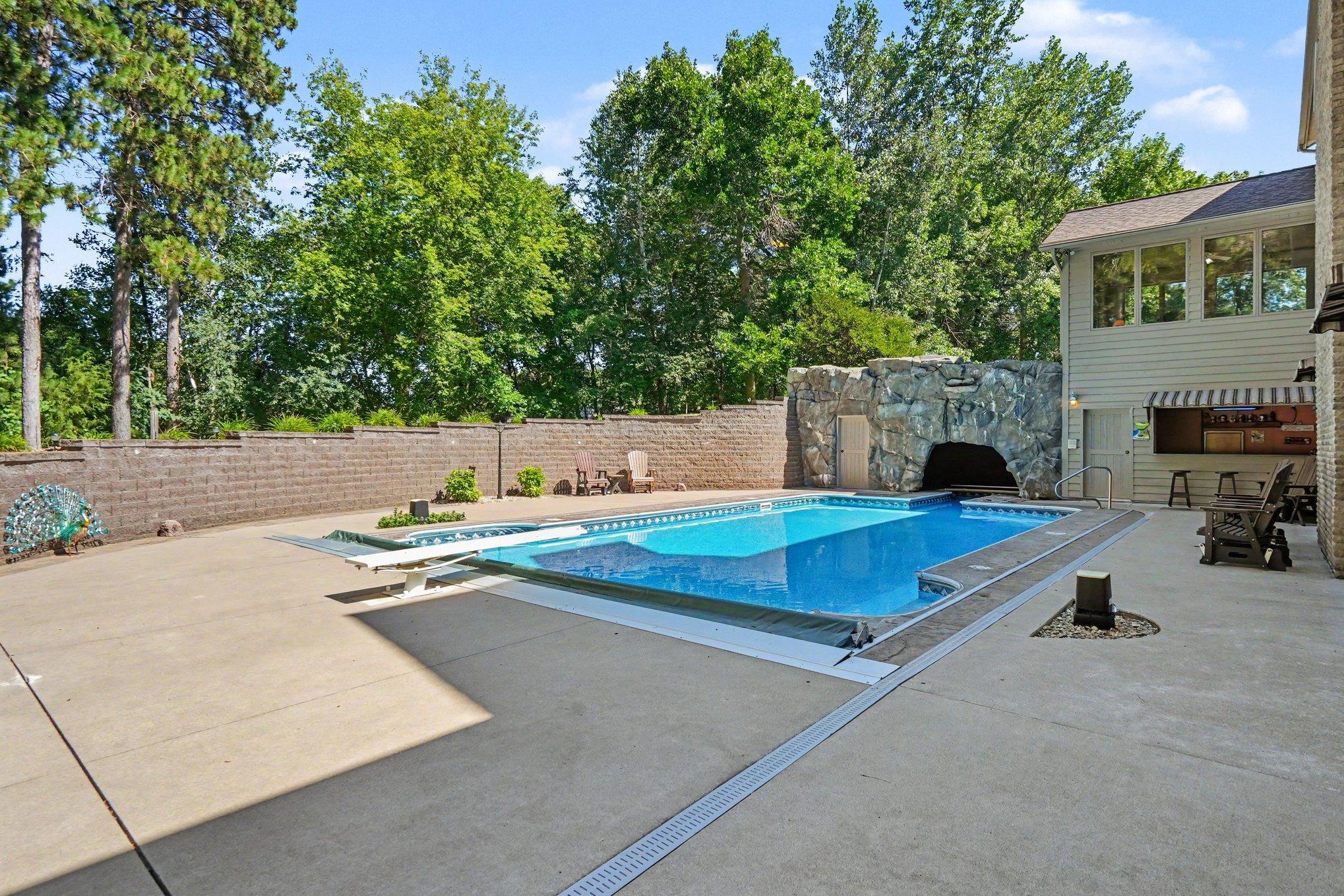 A private in-ground pool is surrounded by generous patio space and mature landscaping, creating a relaxing backyard escape. The distinctive rock grotto adds character while the fully enclosed setting offers exceptional privacy for summer fun.