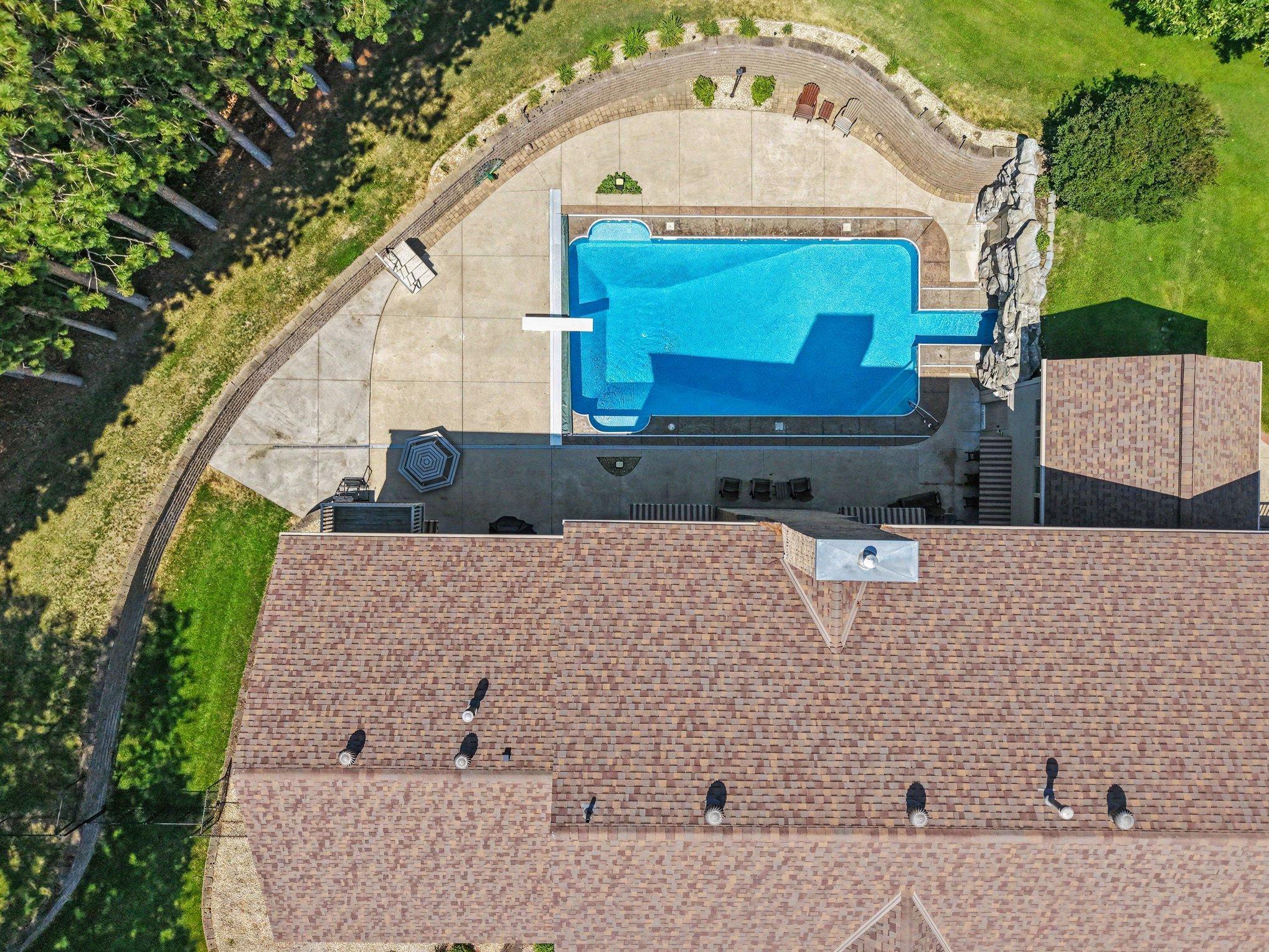 Aerial view showcases the pool’s generous size, expansive patio and private setting surrounded by mature trees. The rock grotto and multiple gathering areas create a resort-like backyard designed for relaxing, entertaining and summer fun.