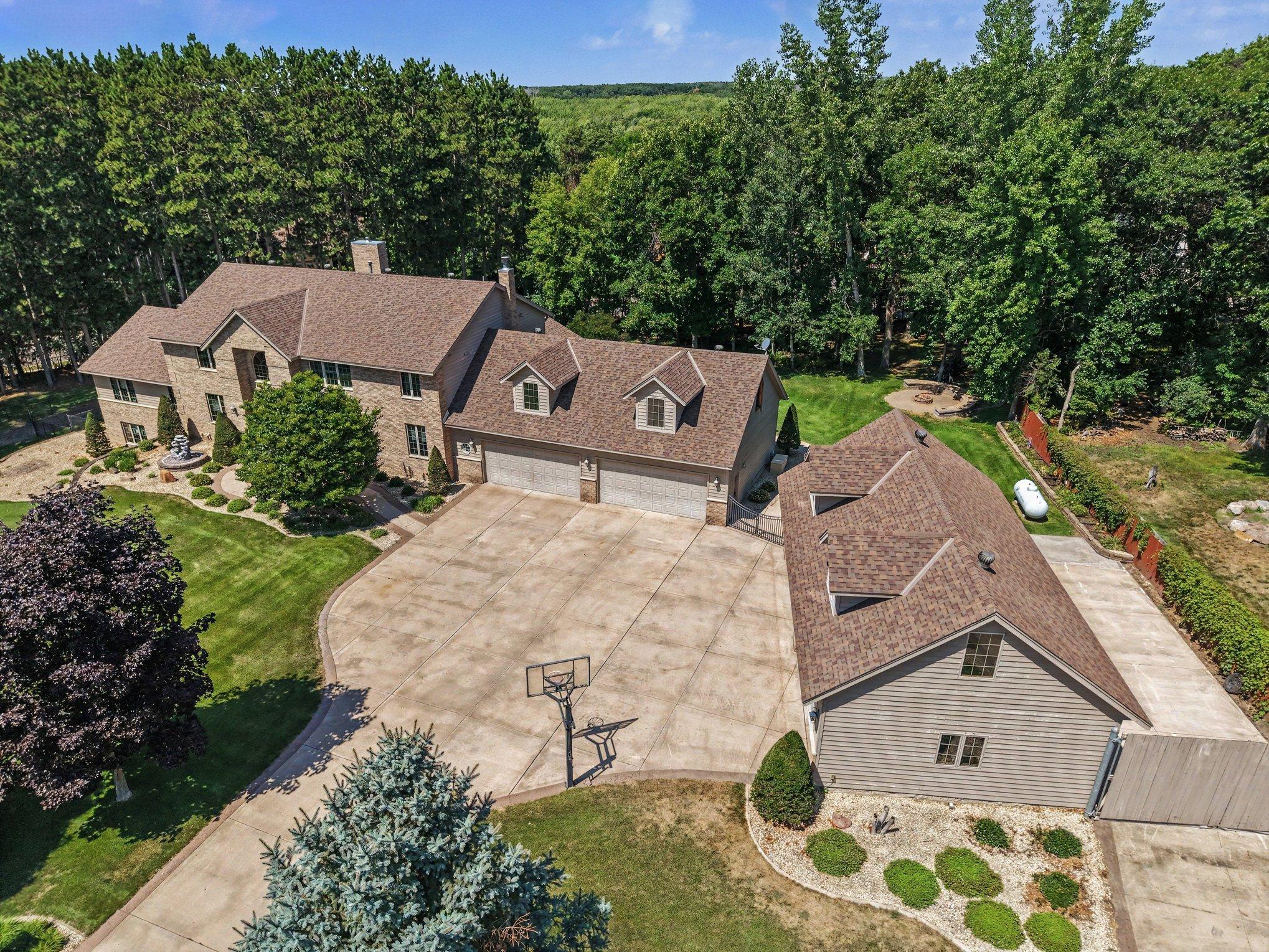 Expansive aerial view showcasing the impressive home, massive driveway and extraordinary garage capacity, all tucked into a private, tree-lined setting. The generous layout offers exceptional space for multiple vehicles, toys, hobbies, etc...