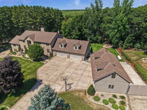 Expansive aerial view showcasing the impressive home, massive driveway and extraordinary garage capacity, all tucked into a private, tree-lined setting. The generous layout offers exceptional space for multiple vehicles, toys, hobbies, etc...