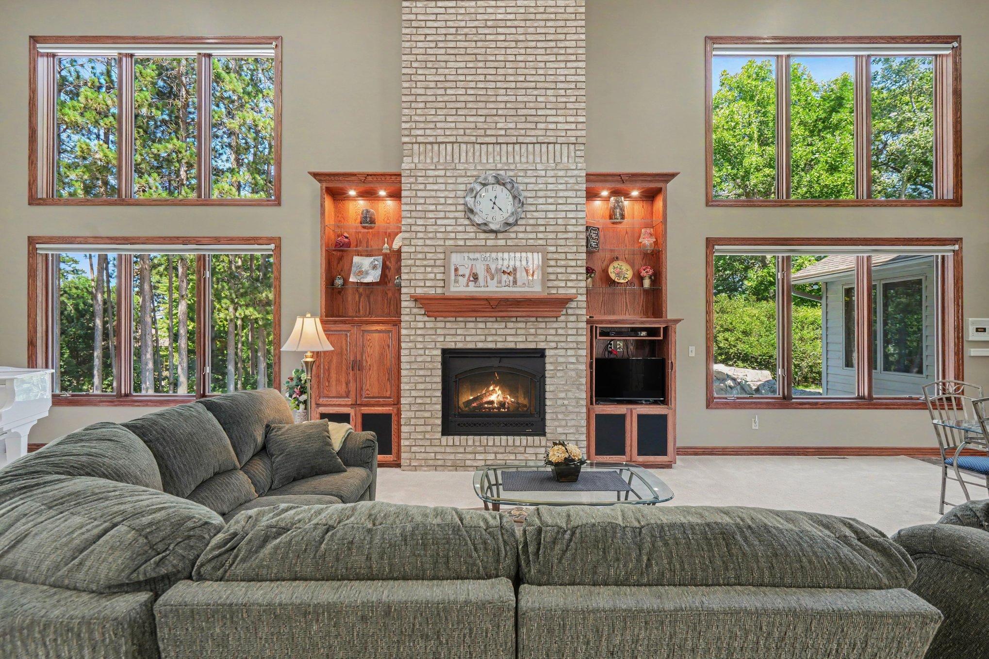 A gas-burning fireplace creates a warm focal point in this inviting living area, flanked by custom built-ins for added character and function. A dramatic wall of windows fills the space with natural light and brings the beauty of the outdoors in.