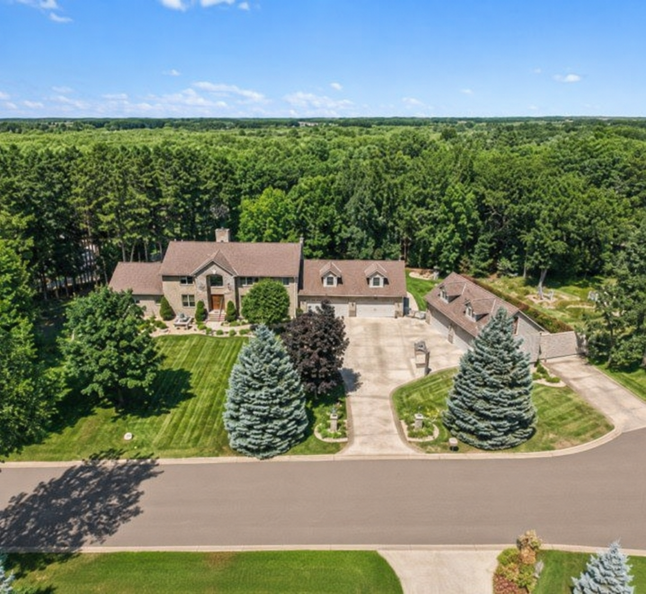 A spectacular aerial view captures the full scale of this one-of-a-kind property, beautifully surrounded by mature trees and sweeping greenery. The impressive home, expansive driveway and dual garage setup create a private estate-like setting.