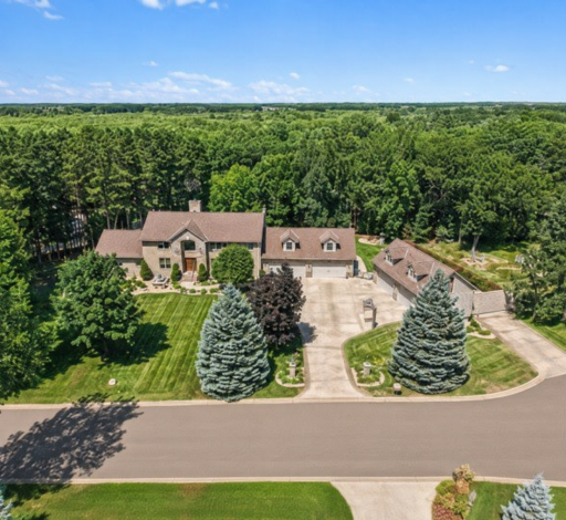 A spectacular aerial view captures the full scale of this one-of-a-kind property, beautifully surrounded by mature trees and sweeping greenery. The impressive home, expansive driveway and dual garage setup create a private estate-like setting.