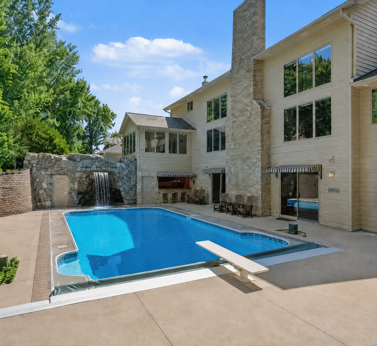 A private backyard retreat featuring an in-ground pool, expansive patio and dramatic rock grotto with a cascading waterfall feature. The multi-level exterior and abundant windows create a beautiful connection between indoor and outdoor living.