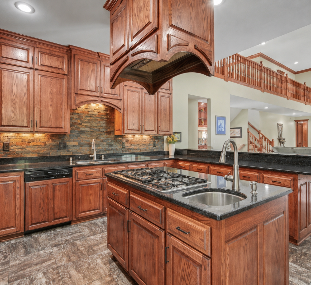 Custom kitchen featuring rich cabinetry, granite countertops, tile floors and a center island with cooktop and prep sink. Open sightlines and beautiful woodwork create a warm, impressive gathering space.
