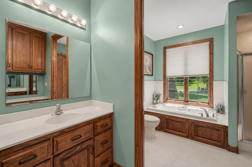 The spacious primary en-suite features dual vanities, abundant cabinetry and a relaxing jetted tub beneath a large window. Warm wood finishes and generous natural light create a comfortable, private retreat.