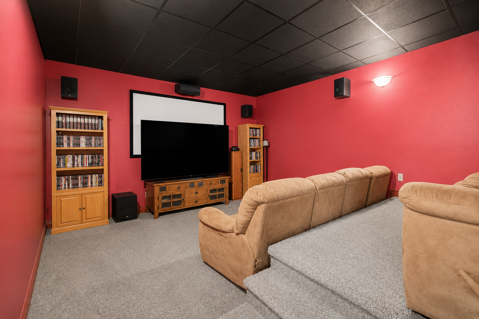 A dedicated lower-level theater room delivers a true movie-night experience with tiered seating, a large screen and built-in media storage. The dark ceiling and bold walls create the perfect atmosphere for films, sports and family entertainment.