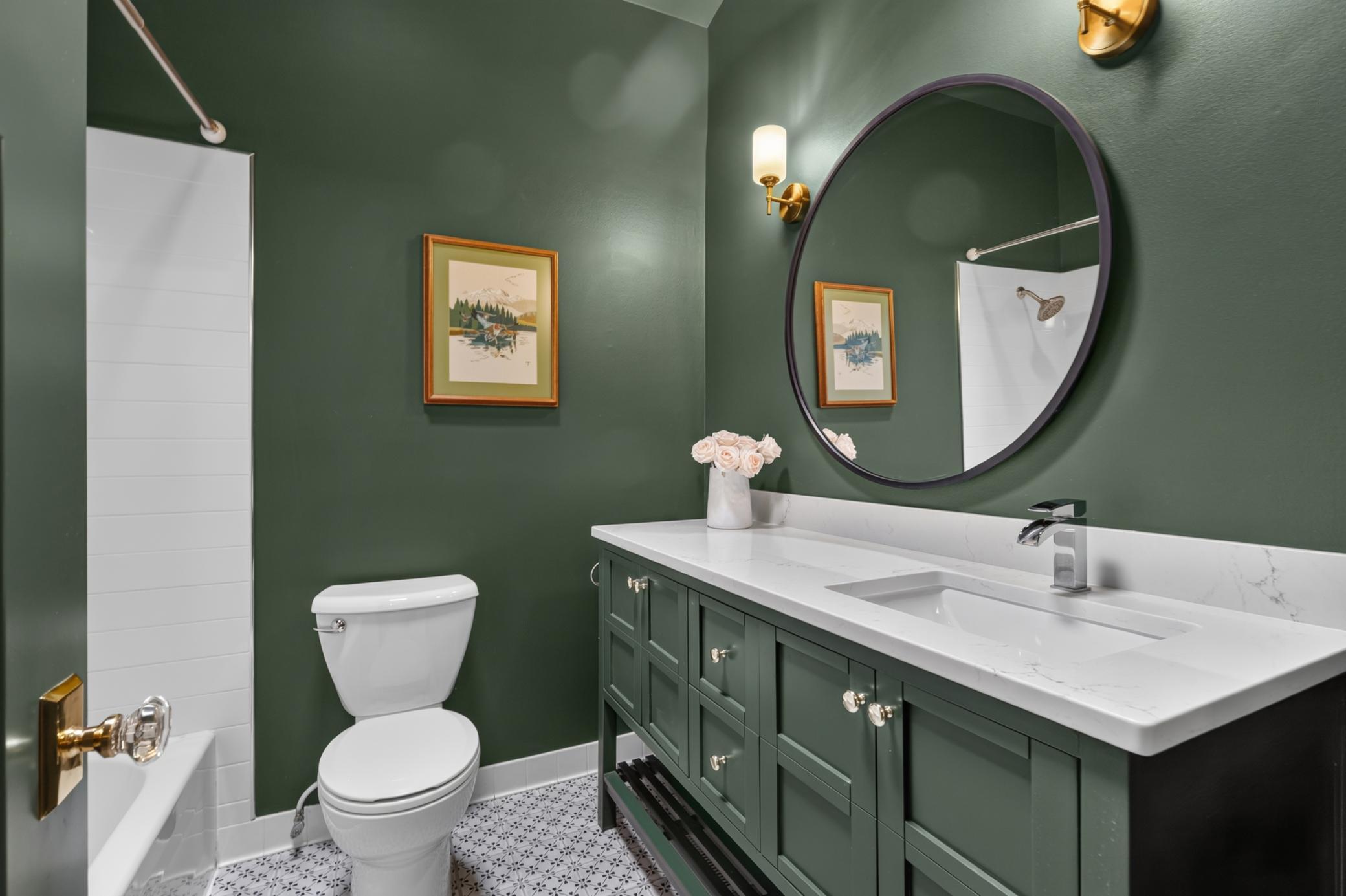 Full Bathroom on the Main Level features enameled vanity cabinet w/ quartz top, vaulted ceilings with skylight, tub surround offers subway tile, linen closet and tile flooring