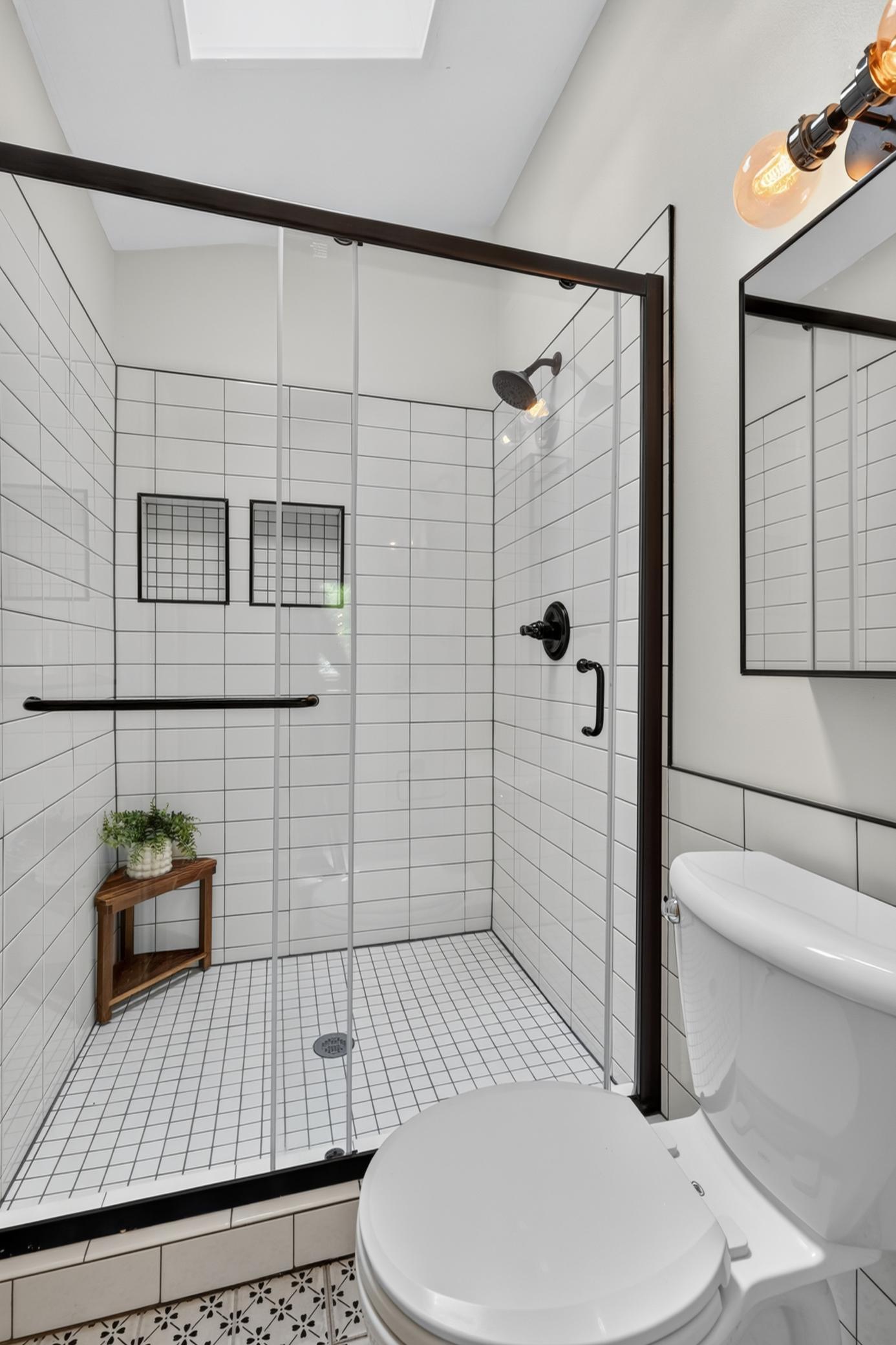 Master 3/4 bathroom features subway tile wainscoting, tile flooring and vaulted ceilings with skylight. Shower offers subway tile surround, shampoo niche and glass enclosure