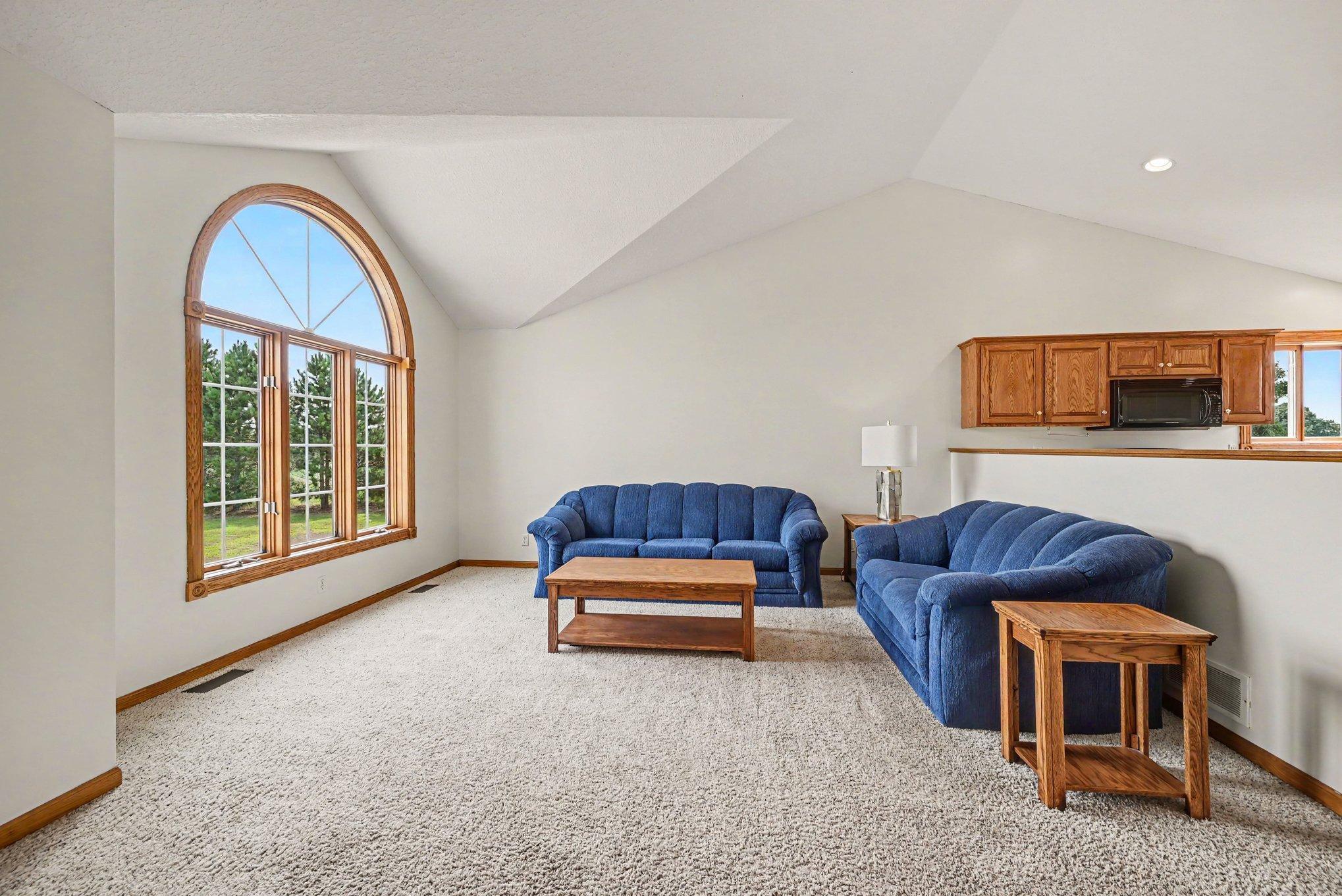 Spacious living room featuring vaulted ceilings and an impressive arched window overlooking the property.