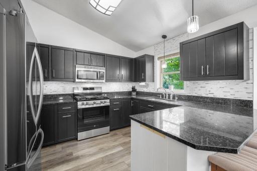 Wow! Gorgeous kitchen featuring classy black cabinetry, Granite countertops, Stainless Steel appliances, and a modern tiled backsplash.