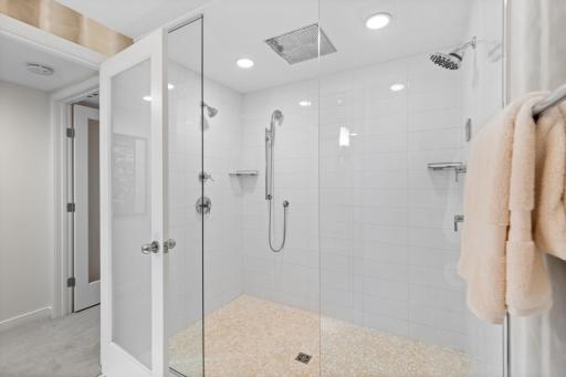 The adjacent bathroom feels spa-like with an expansive tiled walk-in rain shower with dual shower heads.