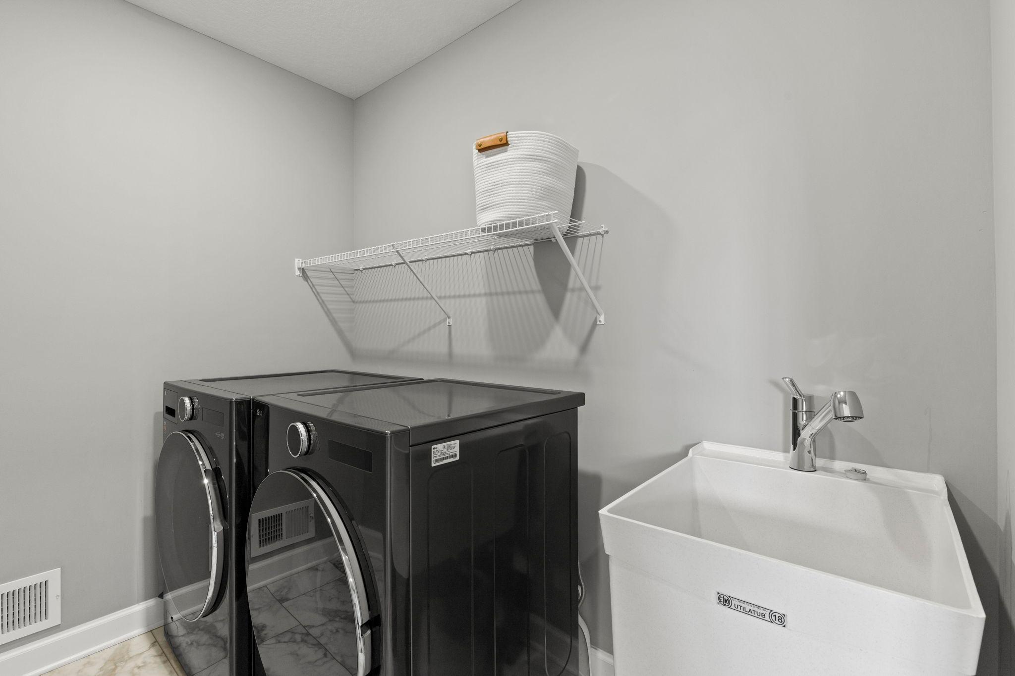 Convenient upper level laundry room, complete with front-loading washer and dryer, utility sink, and wire shelving.