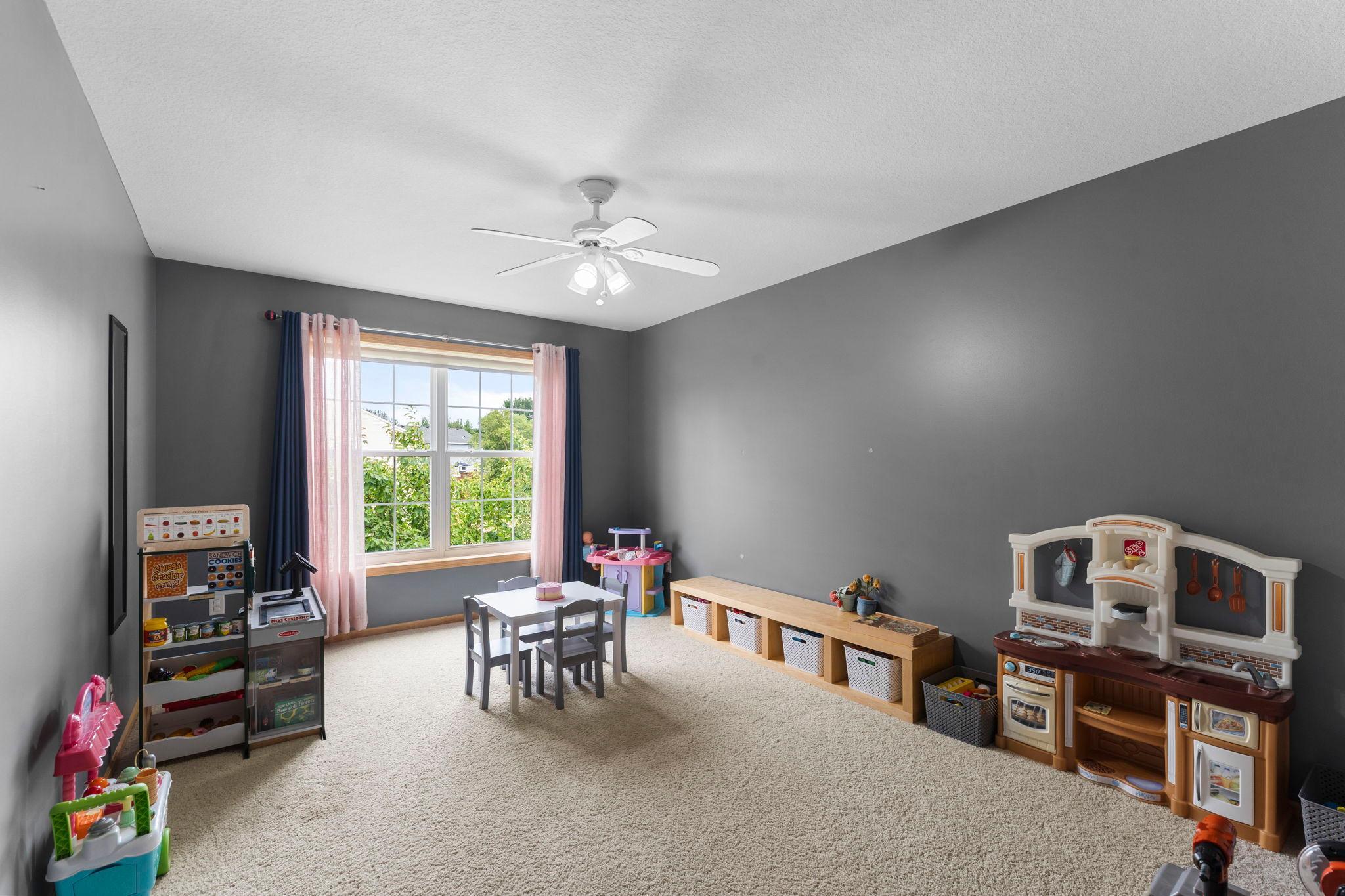 Spacious bedroom four on the upper level offering a large front-facing window, ceiling fan, and ample closet space.