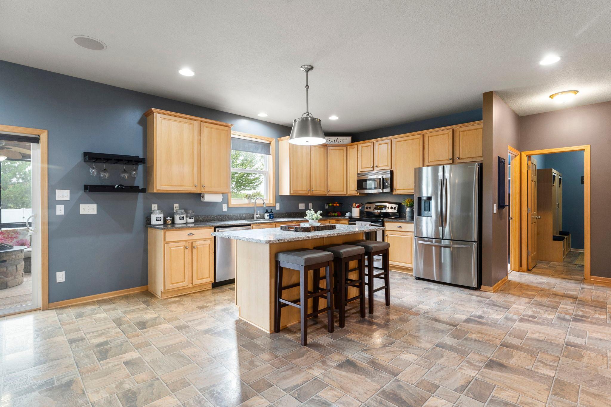 The chef-inspired kitchen features expansive Cambria countertops, a large center island with breakfast bar seating, abundant cabinetry, and stainless steel appliances.