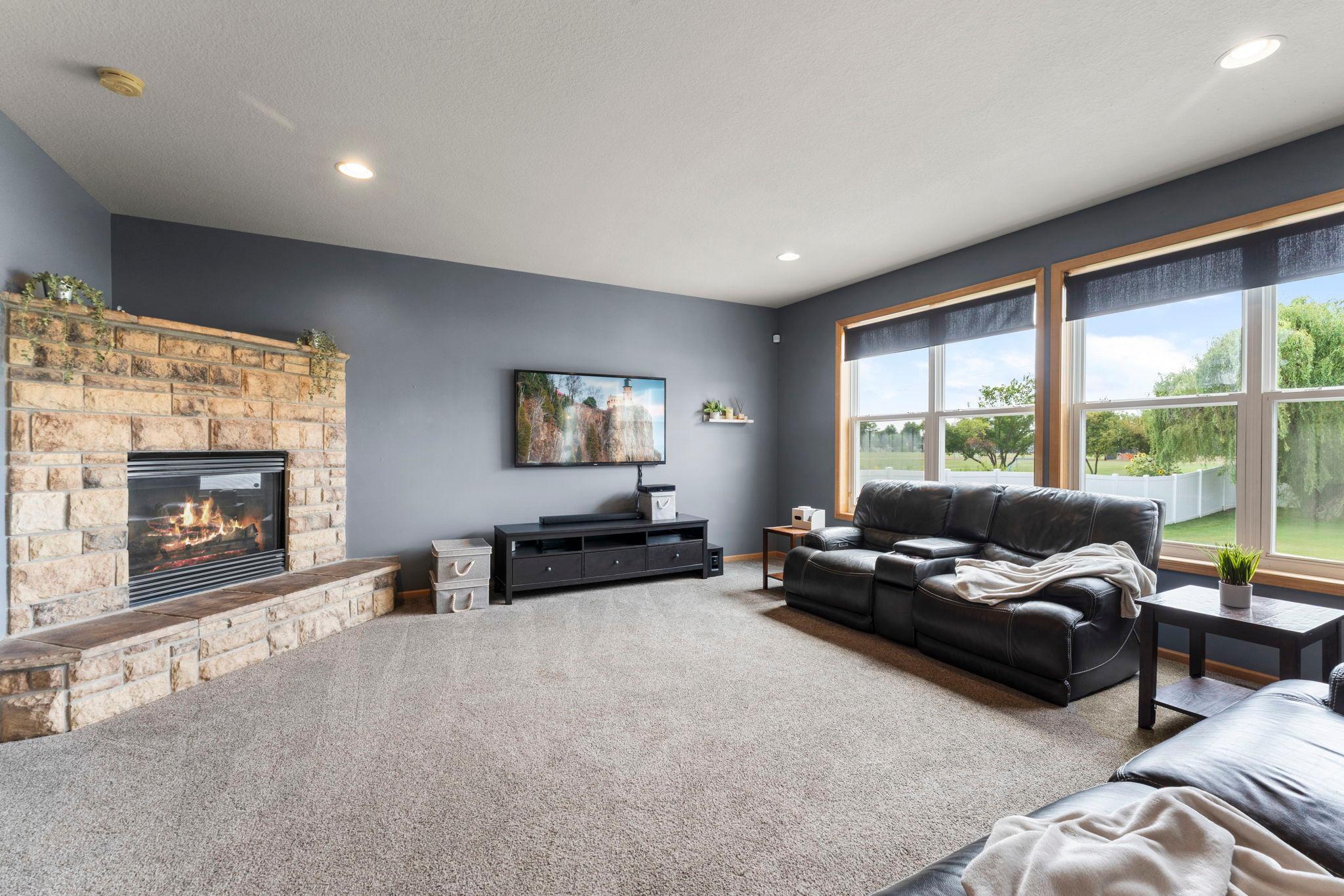 Adjacent to the informal dining area, the spacious main-level living room features plush carpeting, a cozy gas-burning fireplace, and a large window that fills the space with abundant natural light, creating a warm and inviting gathering place.