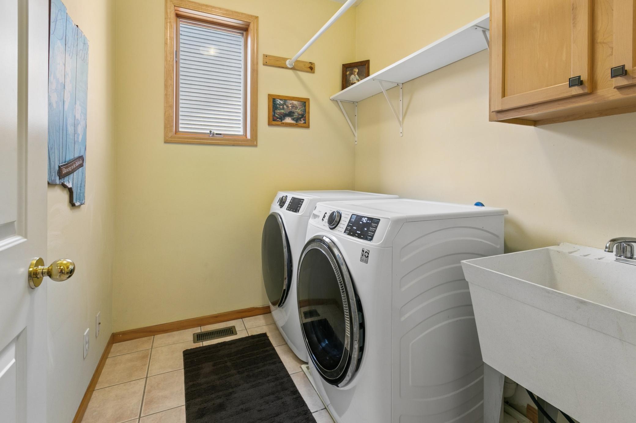 Main-level laundry room with sink and storage. New GE front loading washer and dryer stay with the home.