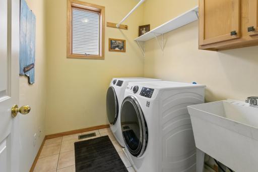 Main-level laundry room with sink and storage. New GE front loading washer and dryer stay with the home.