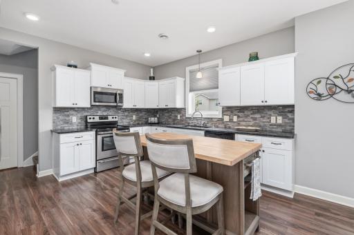 The bright white kitchen includes tons of cabinetry, stainless steel appliances, tile back splash, granite counter tops and center island.