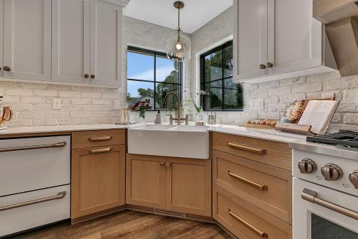 A beautiful kitchen sink area framed by two windows overlooking the backyard, with under-cabinet lighting adding a warm ambiance and inviting glow to the space.