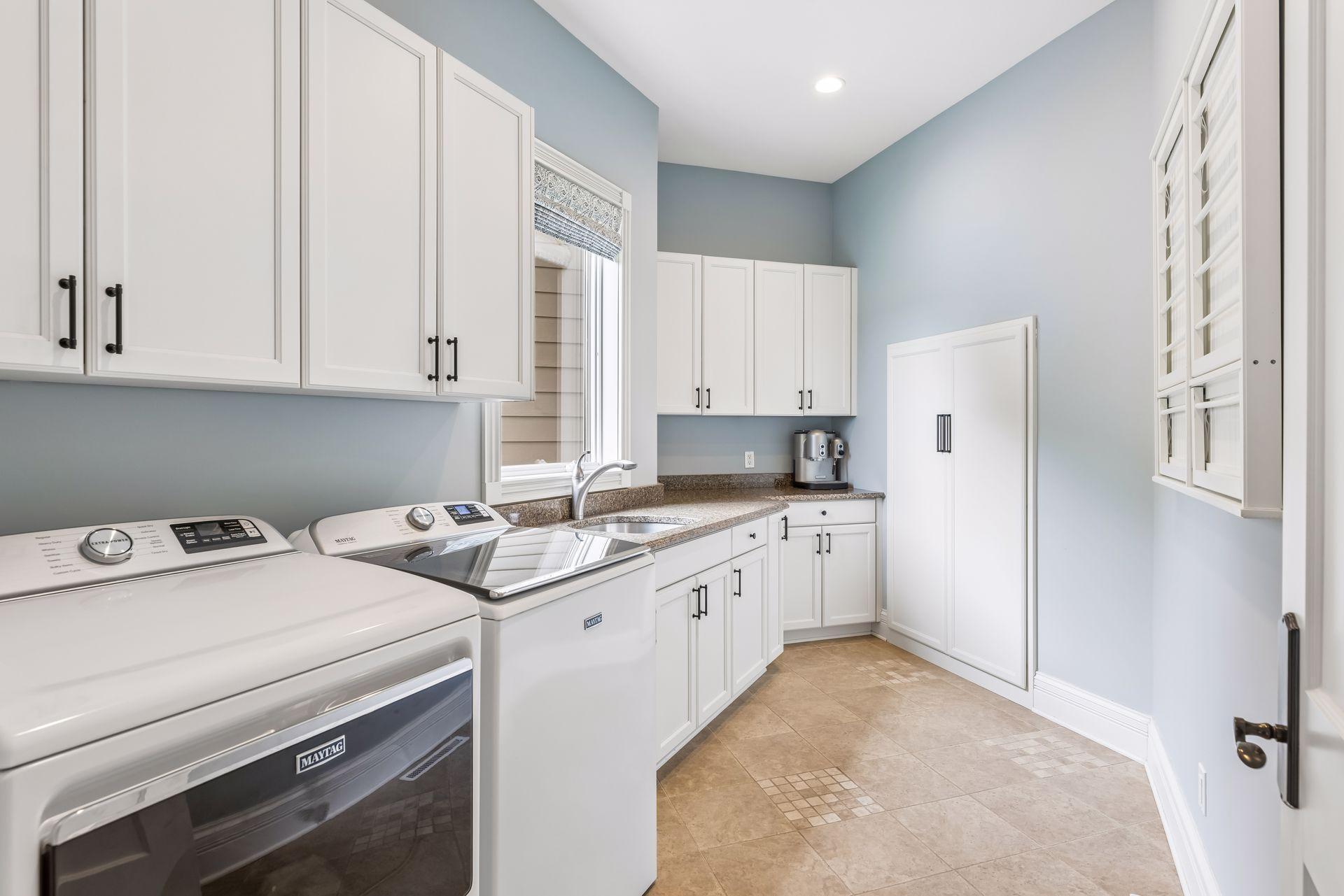 A spacious main-floor laundry room features newer washer and dryer units, permanent drying racks, and a convenient storage closet for brooms, mops, and cleaning supplies.