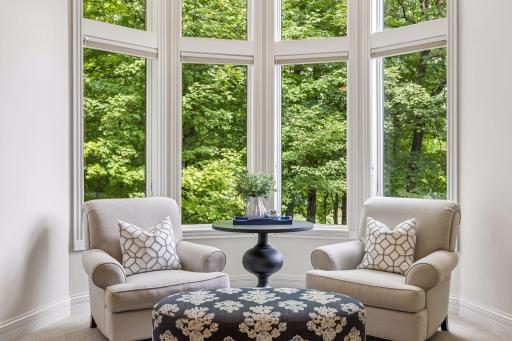 An inviting sitting area in the primary bedroom offers peaceful views of the surrounding trees.