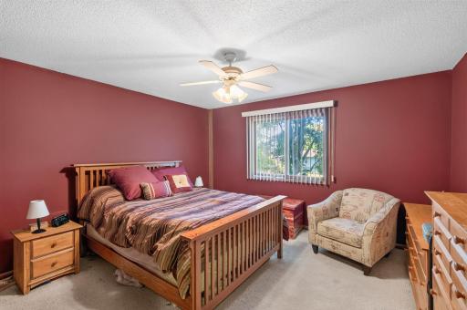 The upper level primary bedroom provides a peaceful personal space with a spacious layout, a ceiling fan for added comfort, and a large window overlooking the outdoors.