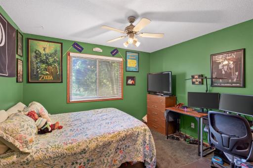The second bedroom on the upper level offers a comfortable retreat with a generous sleeping area, ceiling fan, and plenty of natural sunlight from the large window.