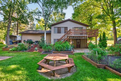 The expansive backyard is ideal for outdoor living, with raised garden beds, mature landscaping, a picnic area, and a spacious deck overlooking the property.
