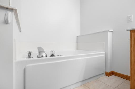 The soaking tub sits right beside the vanity, offering a relaxing retreat within the primary suite. Warm oak cabinetry adds a nice contrast to the light tile.