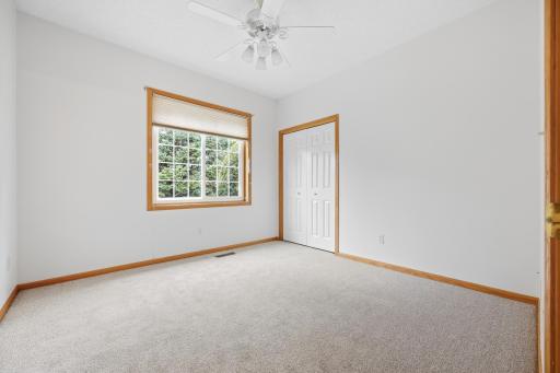 This second bedroom features a large window overlooking mature trees and a spacious closet for storage. A ceiling fan and neutral carpet complete the comfortable space.