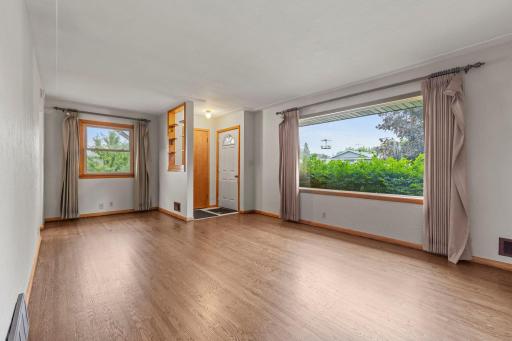 The living room features a large picture window that frames peaceful views of the front yard.
