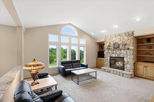 The stunning stone fireplace serves as a beautiful focal point, complemented by custom built-ins and picturesque outdoor views.