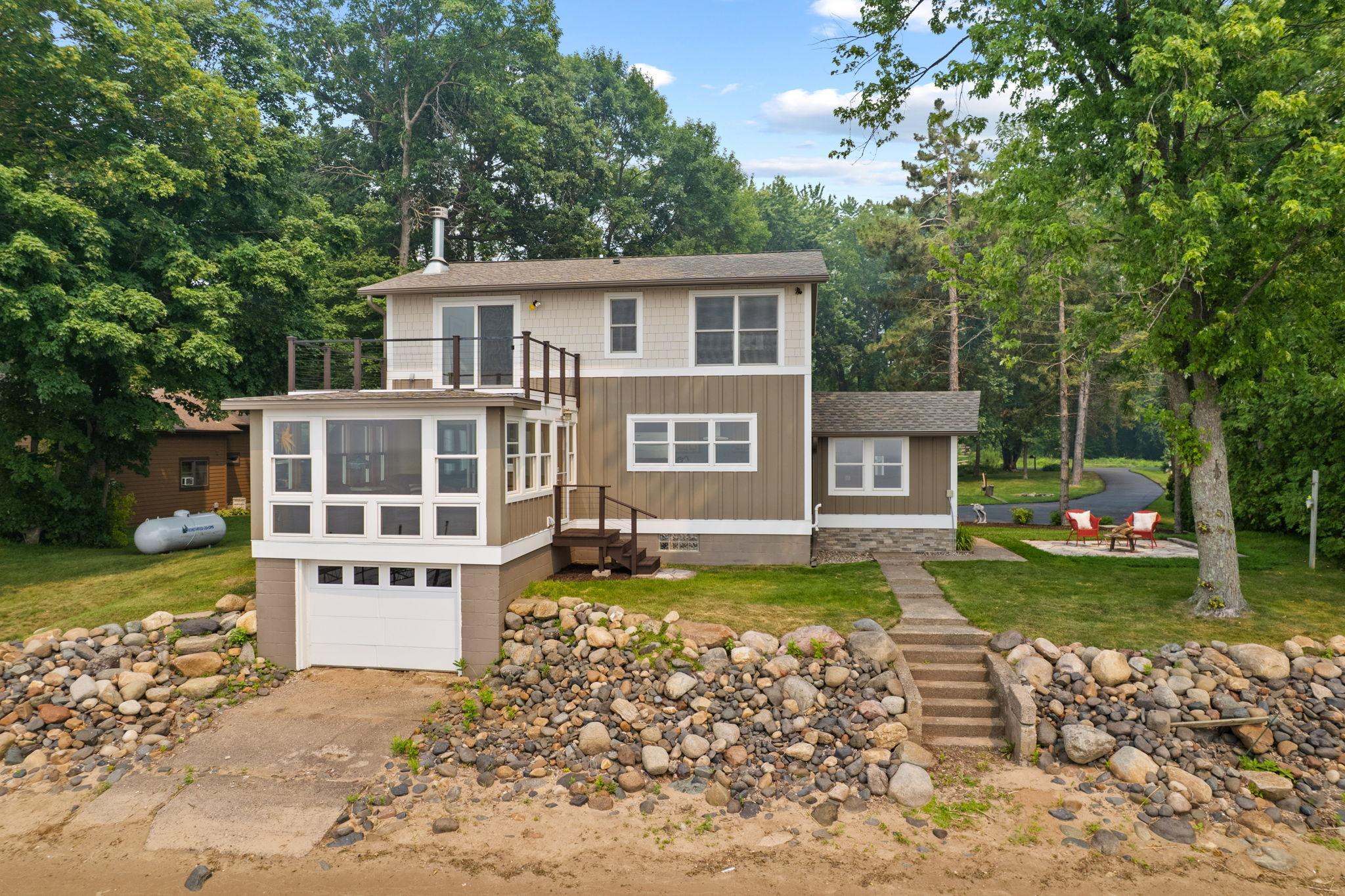 From the shoreline, showcasing the home's architect-designed renovation, four-season sunroom, private owner's deck, and beautifully landscaped setting