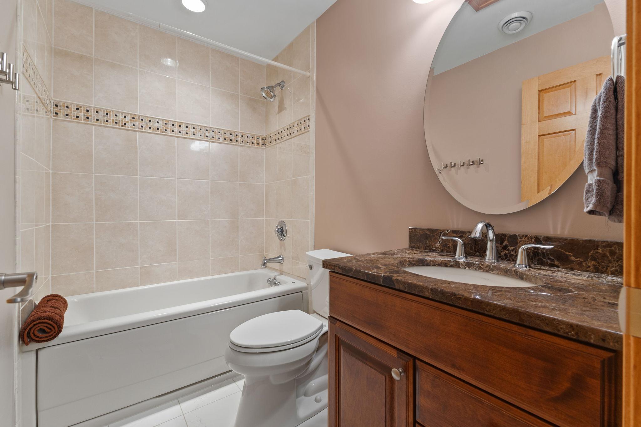 The full guest bath features a beautifully tiled tub/shower surround, stone vanity countertop, and beautiful finishes