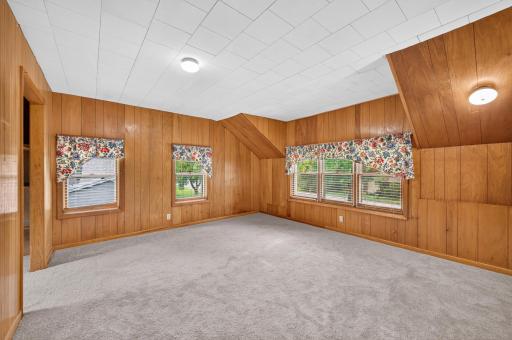 One of three upper-level bedrooms featuring warm wood paneling and multiple windows.