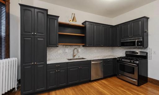 The kitchen was fully-remodeled since the seller purchased the home in 2021, with all new Thomasville 42” arched cabinetry with roll-out shelves and quartzite countertops. The brass-tone sink is topped with floating shelves.