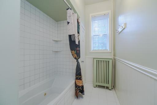 The FULL bathroom is light and bright, with a window, tile flooring, white vanity and wainscoting, and a marble countertop. It has a jetted tub and a closet.
