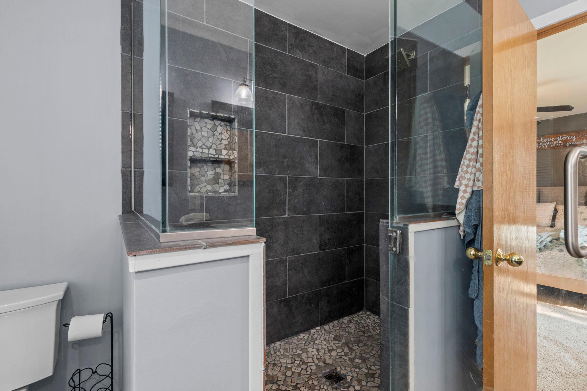 Impressive walk-in shower with glass enclosure, dark tile surround, and pebble-style floor