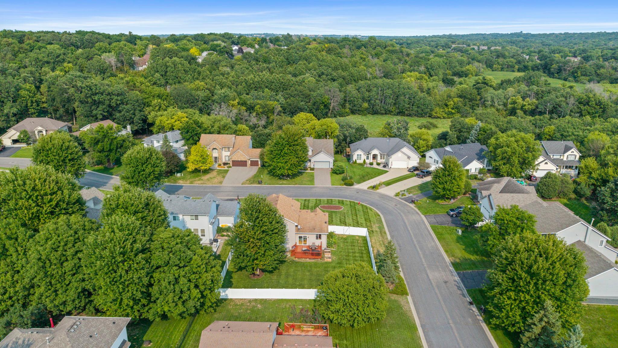 Aerial view showcasing the home’s corner-lot setting and welcoming neighborhood surrounded by mature trees and green space