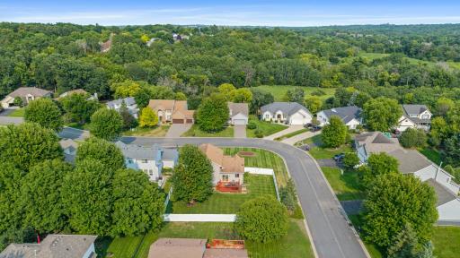 Aerial view showcasing the home’s corner-lot setting and welcoming neighborhood surrounded by mature trees and green space