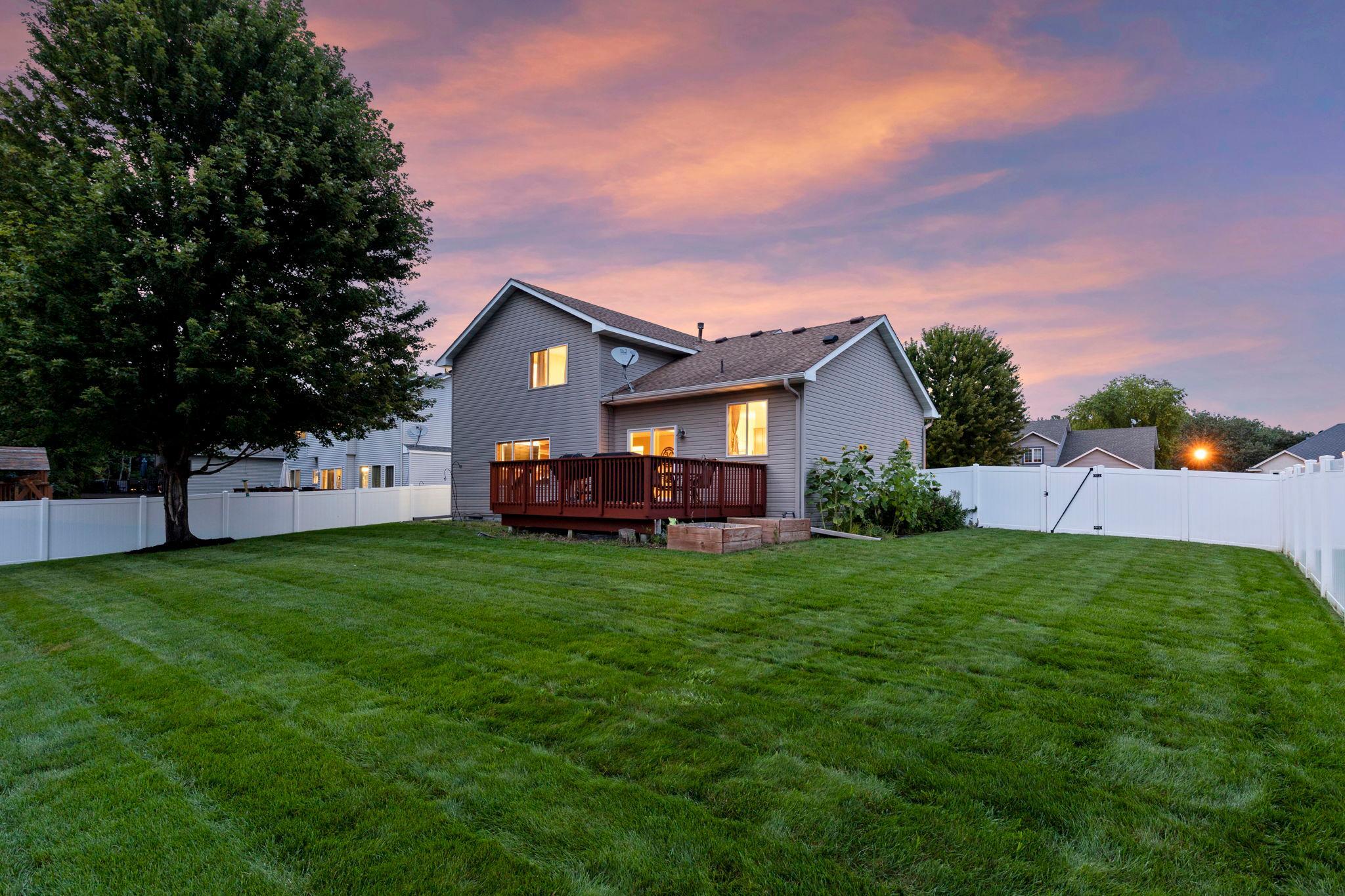 A gorgeous evening view from the backyard, showcasing the new privacy fence, spacious lawn, and deck—plenty of room to relax, play, and entertain