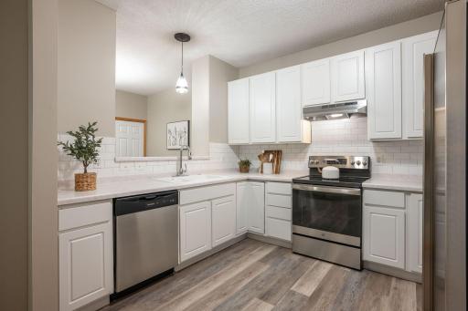 Bright and functional kitchen featuring white cabinetry, stainless steel appliances, subway tile backsplash, and an open pass-through overlooking the dining area.