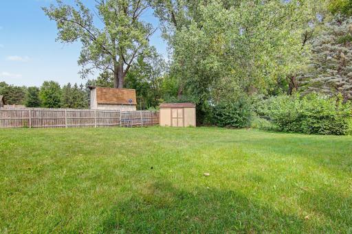 Another view of the spacious backyard with a storage shed and mature landscaping.