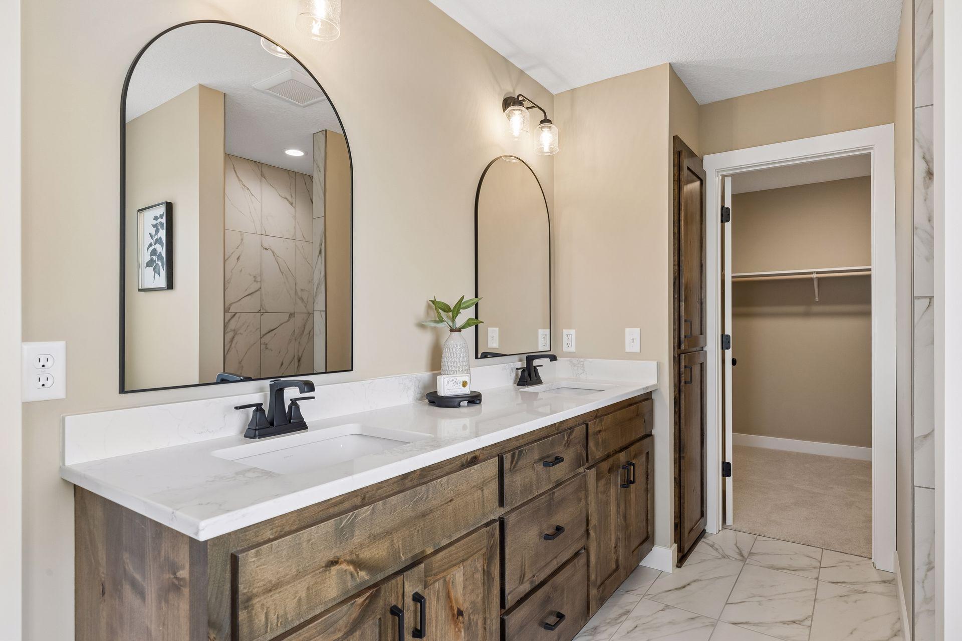 Curved mirrors, stylish tile floors, and a spacious dual sink vanity come together to create a primary bath that feels both sophisticated and functional.
