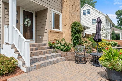 Paver steps and patio create a welcoming approach to the front entry, framed by lush seasonal plantings.