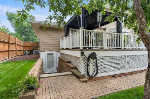 The walkout lower level's door and paver patio sit just beneath the deck, framed by the fully fenced backyard.