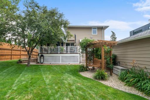 A full view of the fenced backyard showcases the deck, pergola swing, and beautifully maintained lawn.